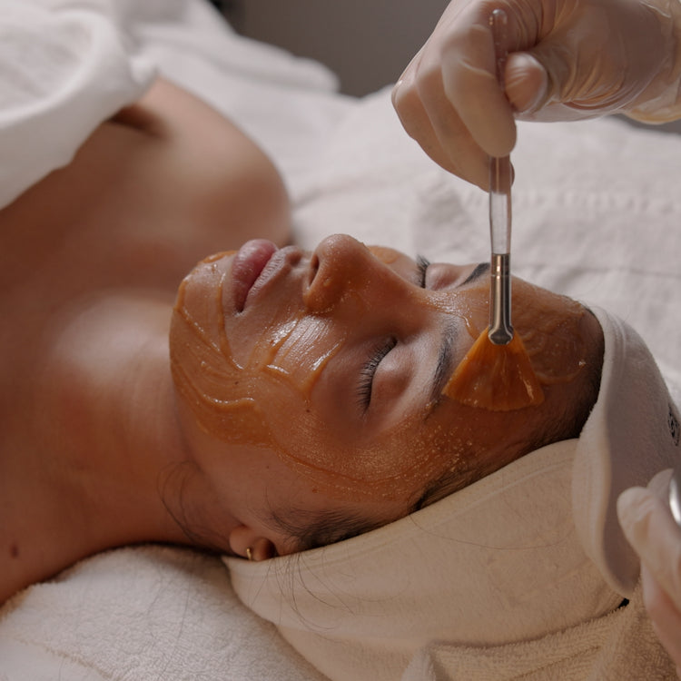 Person receiving a facial treatment with a brush applying a pumpkin mask to their face. Perfect for the fall season.