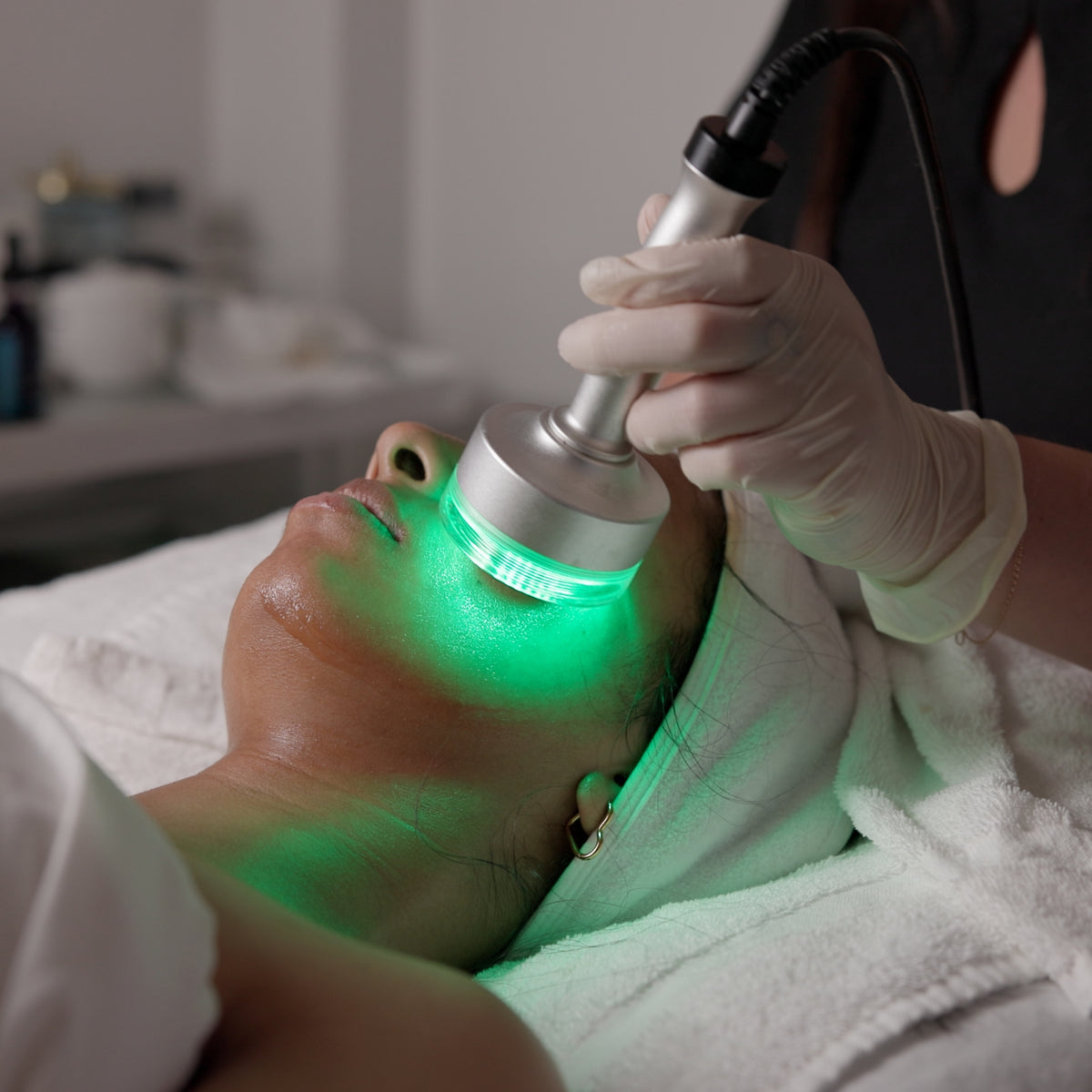 Person receiving a facial treatment with a green led light device in a clinical setting. Myosonix technology.